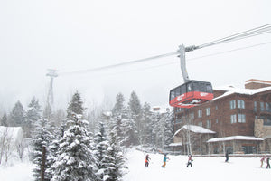 Jackson Hole aerial tram carrying skiers above snowy trees and lodges on a winter day in Teton Village, Wyoming – Nomad Sports.