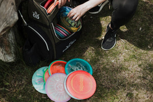 Close-up of a disc golf player selecting colorful discs from a Dynamic Discs bag on a grassy field in Teton Village, Wyoming – Nomad Sports.