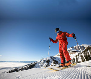 Skier in red Gore-Tex pants and jacket, navigating snowy slopes of Jackson Hole with mountains in the background on a sunny day.