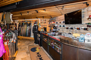 Inside Nomad Sports ski shop in Teton Village, Wyoming, featuring a selection of skis, poles, helmets, goggles, and winter gear displayed neatly on racks and shelves.