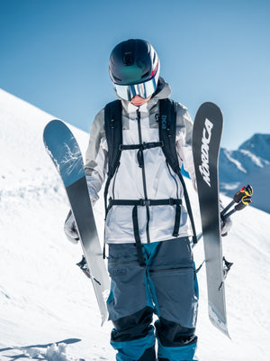 Skier in full gear holding Nordica skis and ski poles on a snowy mountain under a clear blue sky, Teton Village, Wyoming – Nomad Sports.